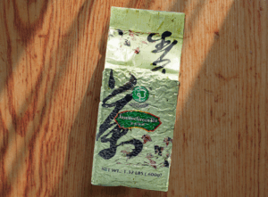 A sealed pack of POSSMEI Jasmine Green Tea placed on a wooden surface with soft sunlight and shadows.