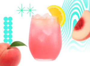 A chilled glass of Fyzzie Pink Peach Lemonade served with ice cubes and a lemon slice, with fresh peach accents around the drink.