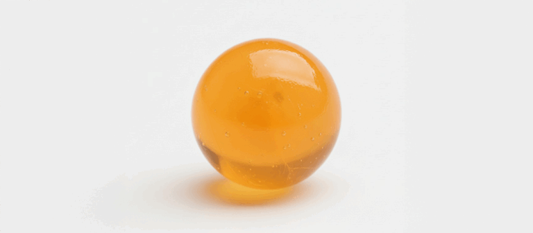A close up of a single orange popping boba ball filled with real fruit juice on a white background.
