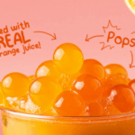 A close up of orange popping boba in a drink filled with real orange juice, highlighting the juicy burst and playful texture, perfect for milk tea shops in the Philippines.