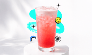 A refreshing Berry Lemon Twist Recipe drink in a tall glass with ice and light foam, placed on a white podium with a bright aesthetic background