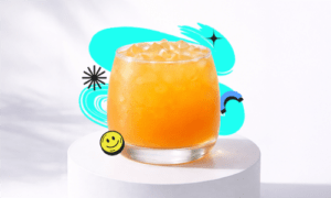 A refreshing Iced Mango Peach drink in a short round glass with ice placed on a white podium with a bright aesthetic background