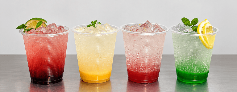 Four colorful iced beverages in clear cups displayed on a café counter, showcasing different drink flavors, colors, and garnishes.
