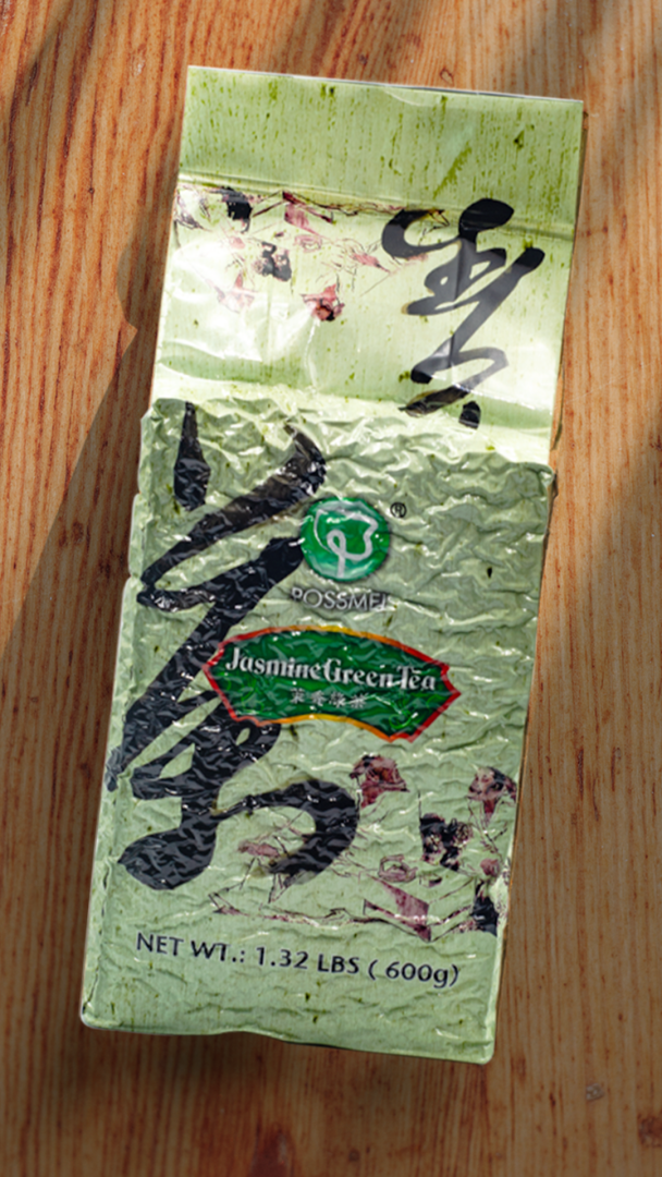 A sealed pack of POSSMEI Jasmine Green Tea placed on a wooden surface with soft sunlight and shadows.